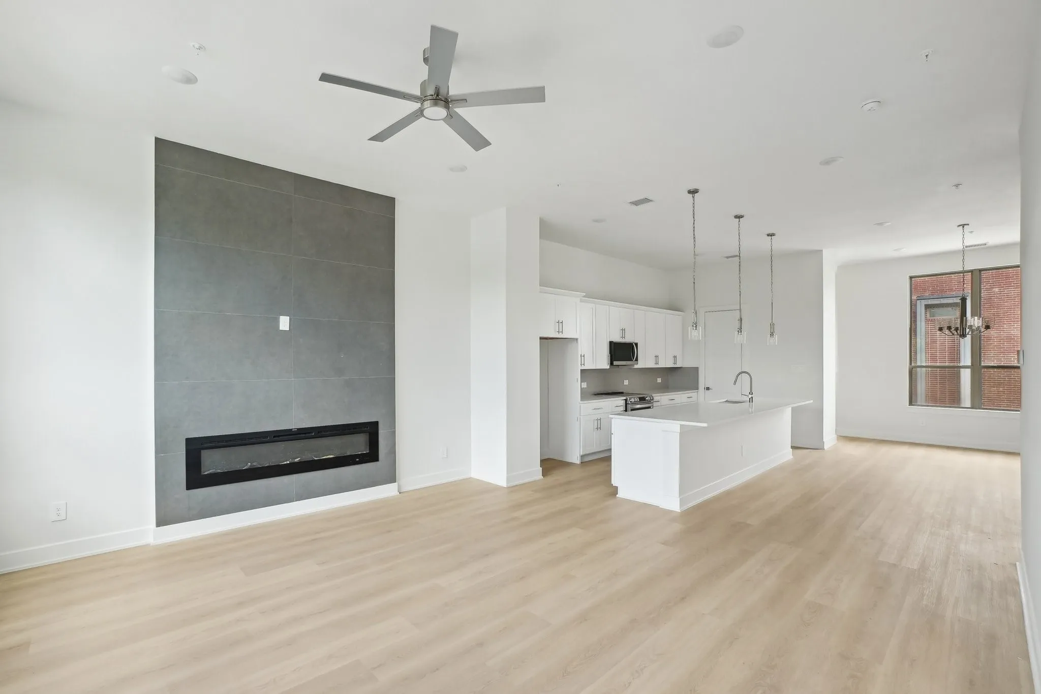 Unfurnished living room with a large fireplace, light wood-type flooring, a ceiling fan, and a chandelier