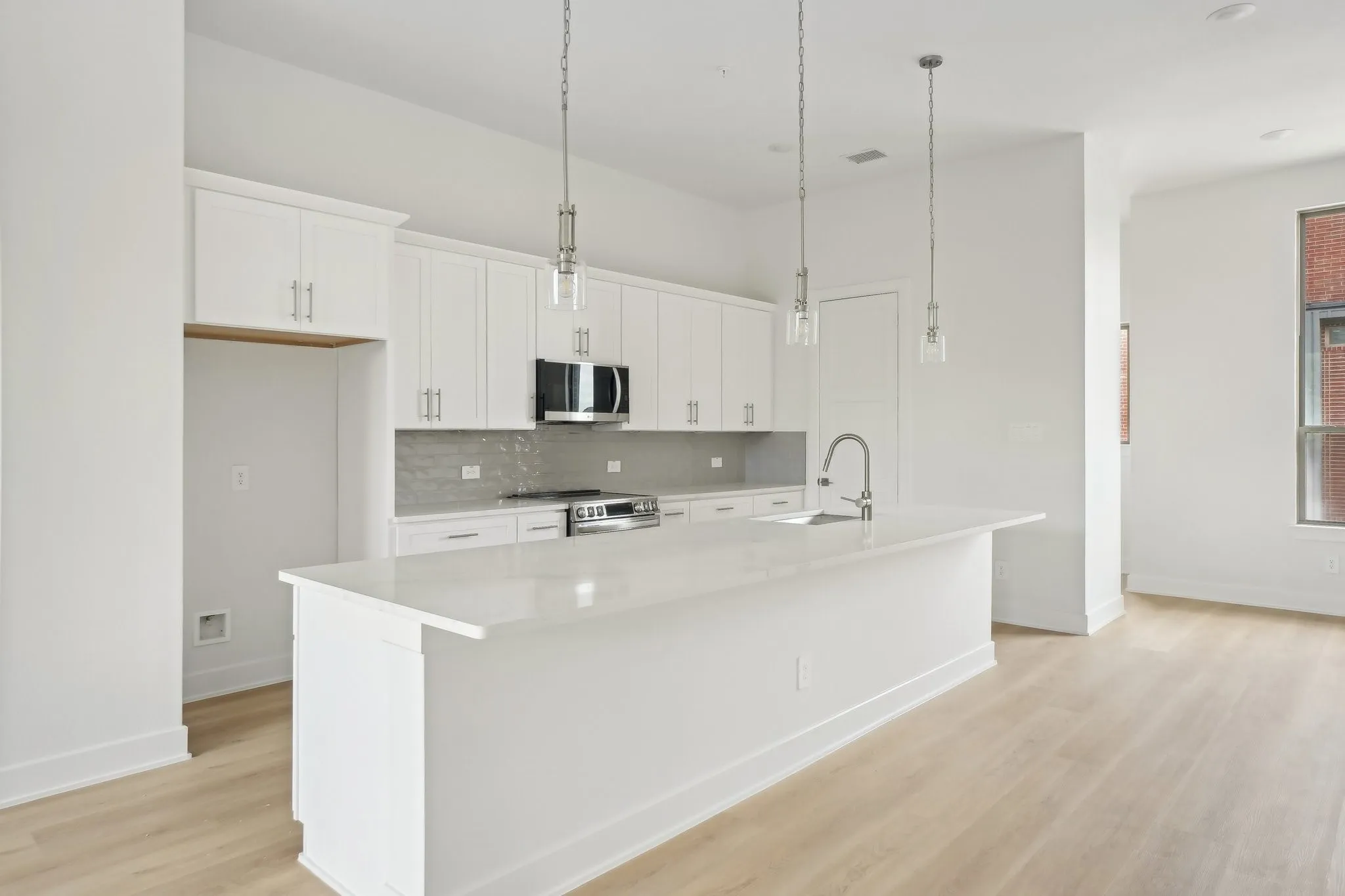 Kitchen with hanging light fixtures, white cabinets, an island with sink, appliances with stainless steel finishes, and light wood finished floors