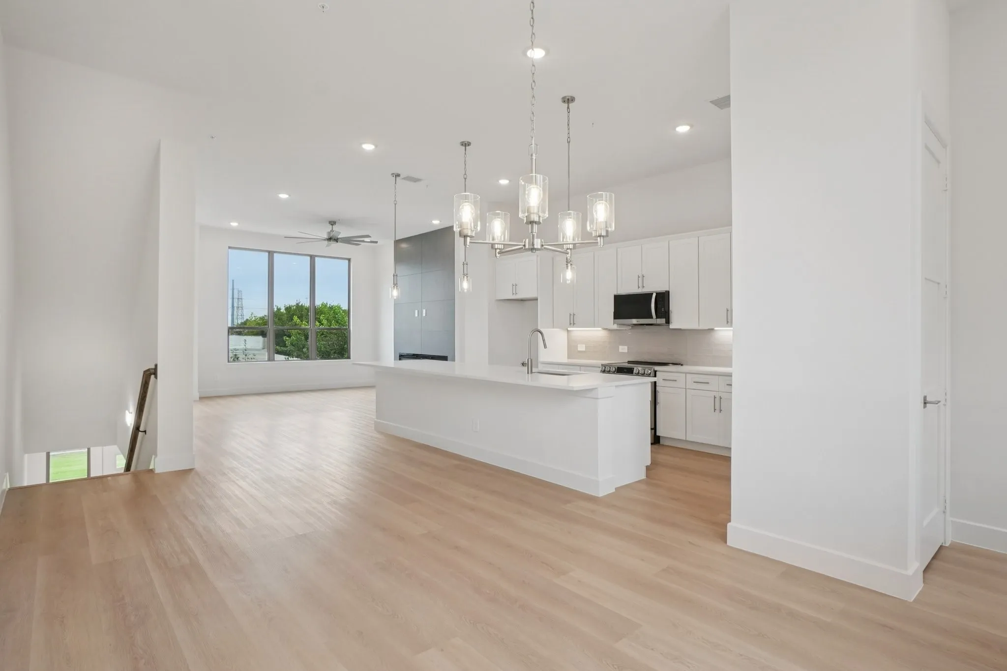 Kitchen featuring open floor plan, a chandelier, a kitchen island with sink, white cabinetry, and pendant lighting