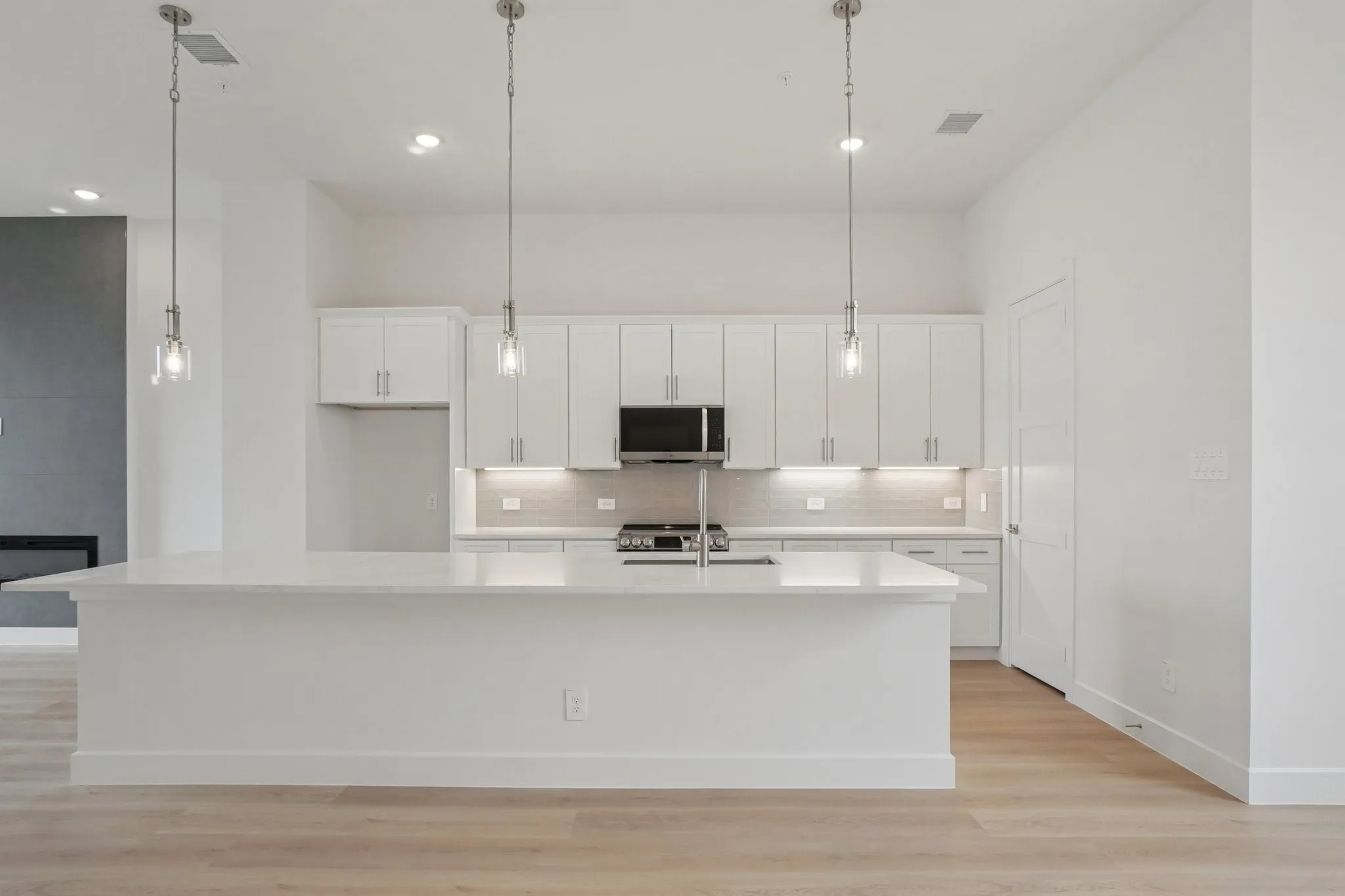Kitchen with white cabinets, a large island with sink, light wood-style floors, pendant lighting, and recessed lighting