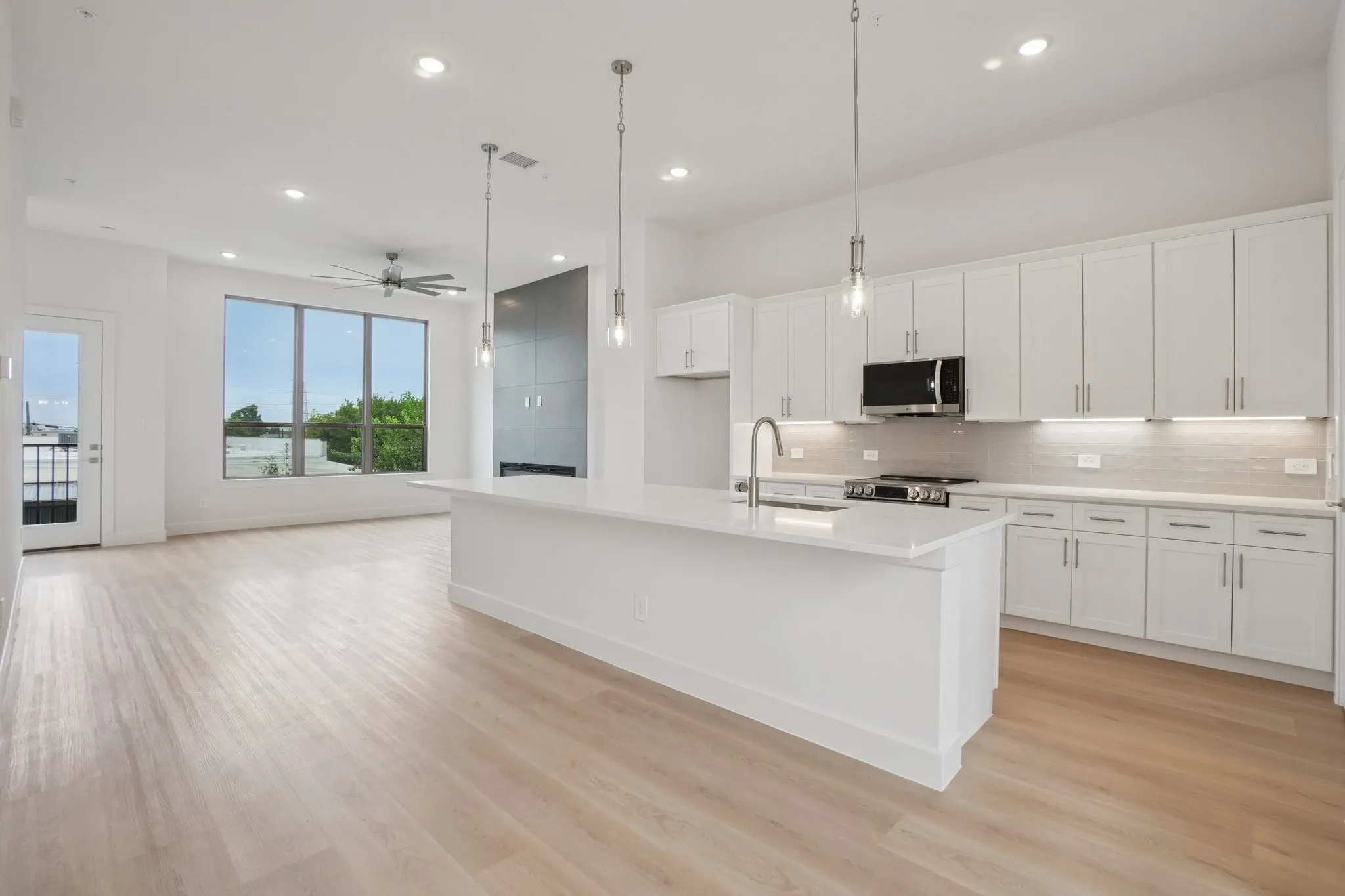 Kitchen featuring hanging light fixtures, white cabinetry, a center island with sink, light wood finished floors, and recessed lighting