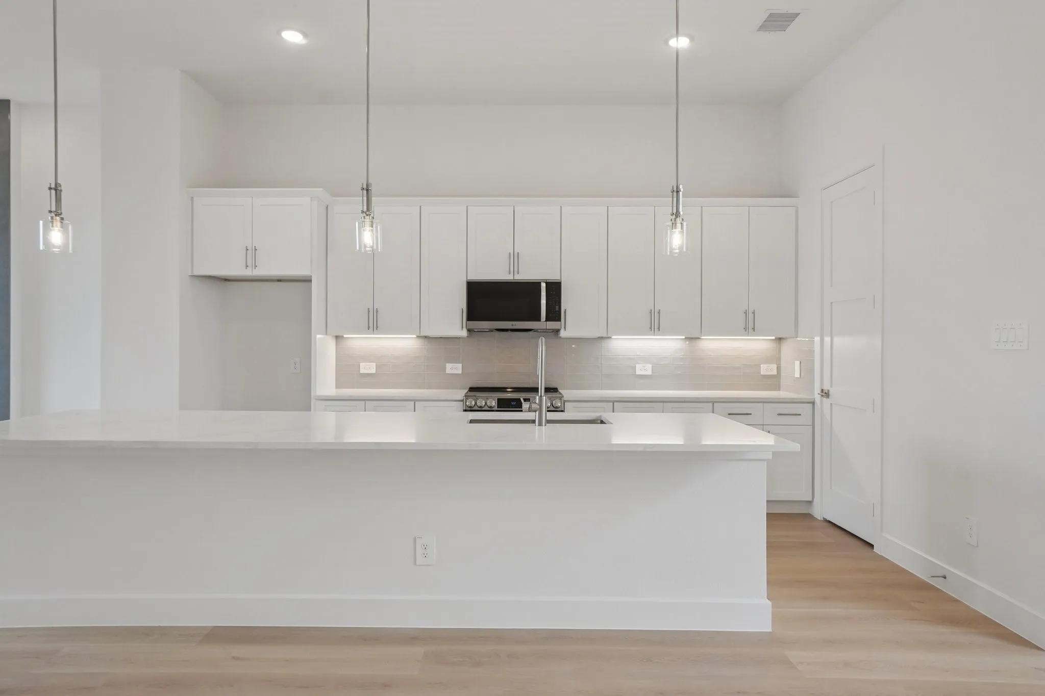 Kitchen featuring white cabinetry, light wood-style floors, a spacious island, pendant lighting, and light stone countertops