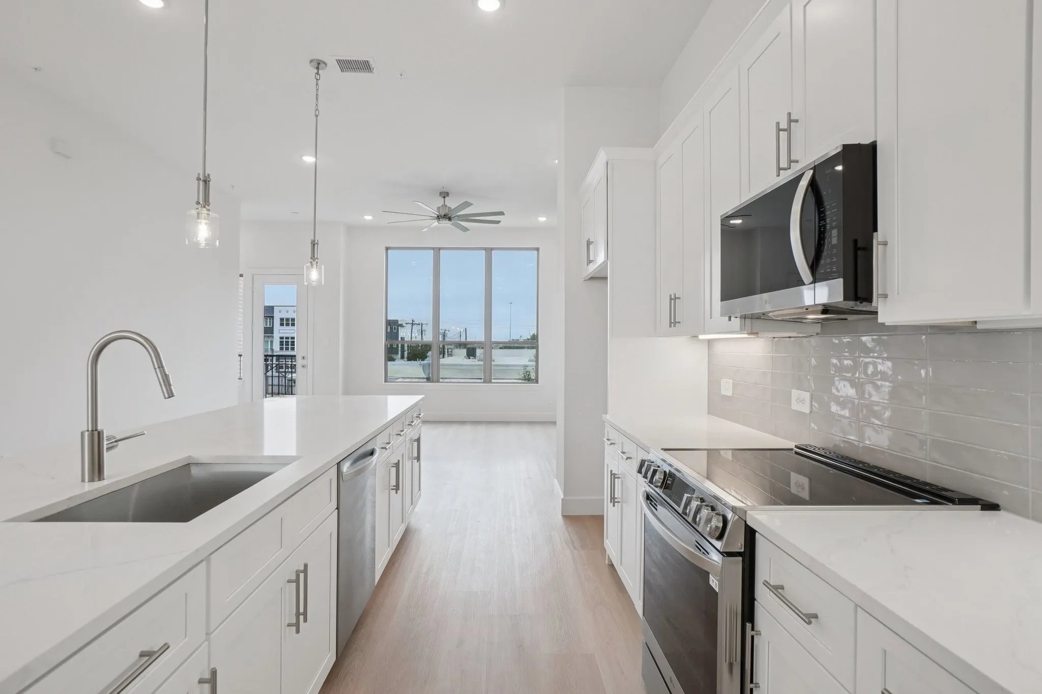 Kitchen featuring appliances with stainless steel finishes, white cabinetry, pendant lighting, light stone counters, and light wood-style flooring