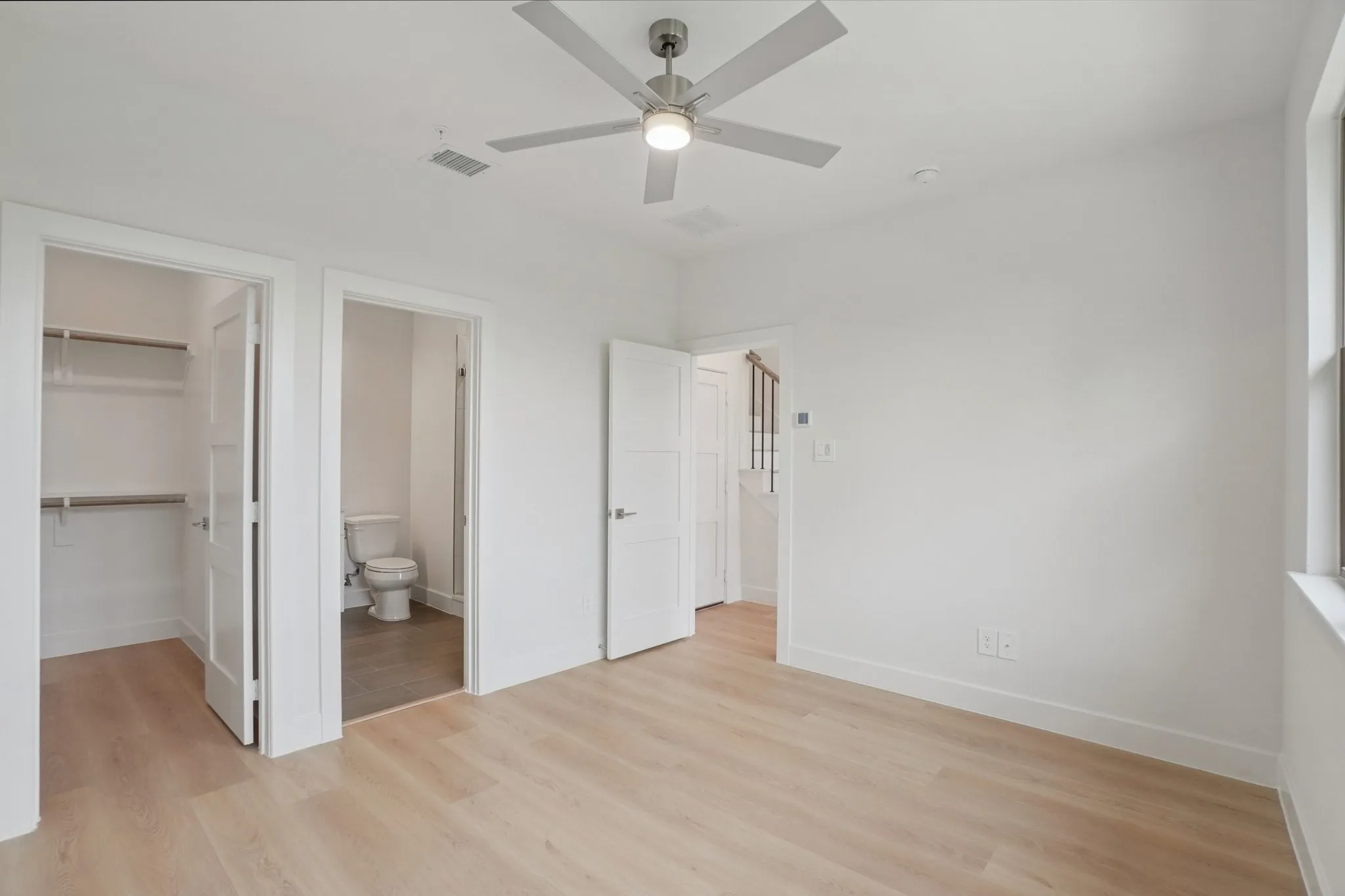 Unfurnished bedroom with a spacious closet, light wood-style floors, a ceiling fan, and connected bathroom