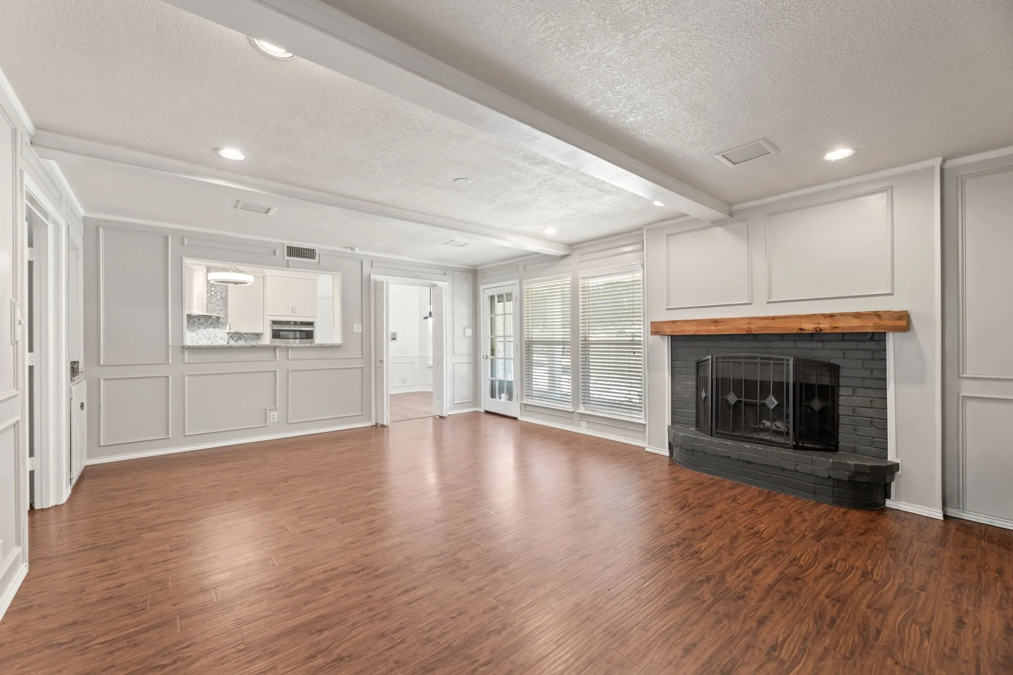 Unfurnished living room with a decorative wall, a textured ceiling, dark wood-style flooring, a fireplace, and beam ceiling