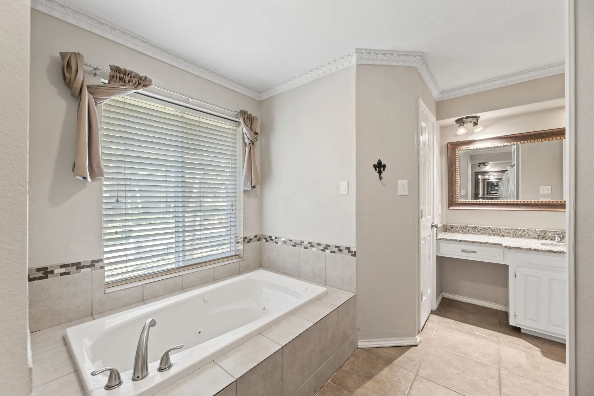 Bathroom with a jetted tub, vanity, light tile patterned flooring, and crown molding