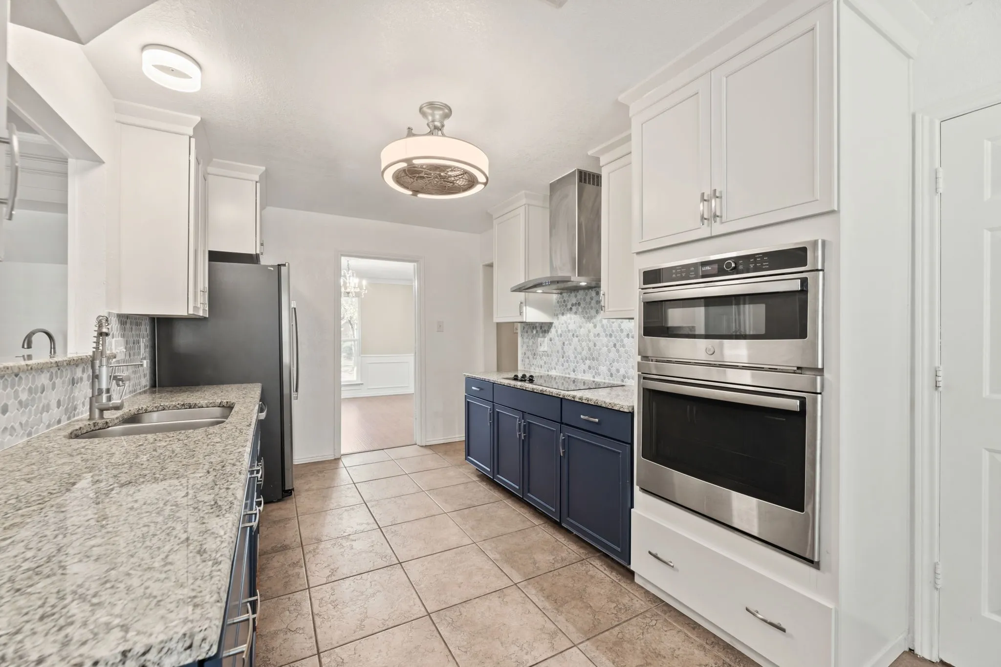 Kitchen featuring appliances with stainless steel finishes, white cabinets, blue cabinets, wall chimney exhaust hood, and light stone counters