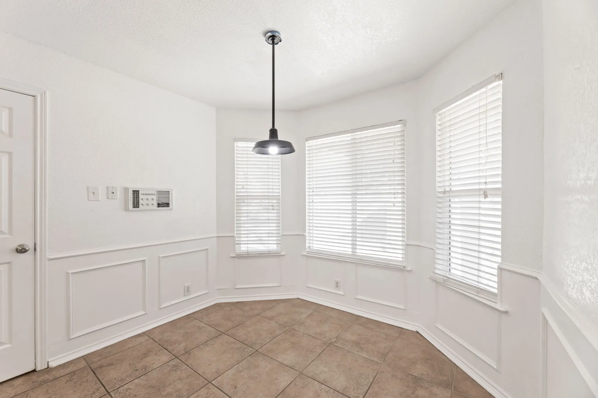 Unfurnished dining area with wainscoting, a decorative wall, tile patterned floors, and a textured ceiling