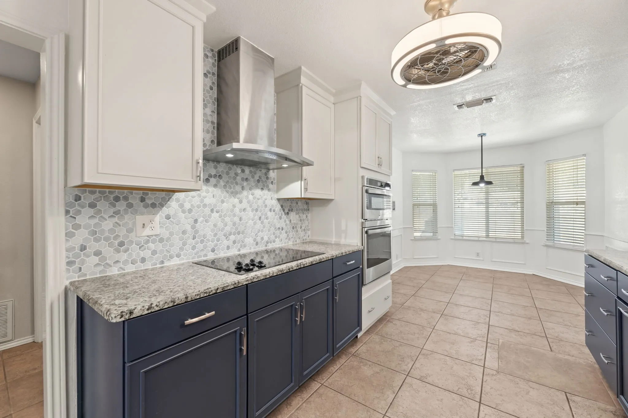 Kitchen with hanging light fixtures, tasteful backsplash, wall chimney range hood, white cabinetry, and blue cabinetry