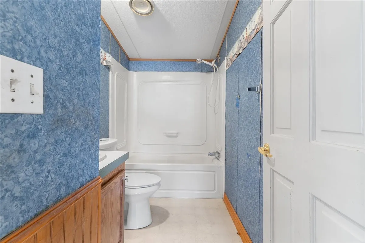 Bathroom with bathtub / shower combination, vanity, wallpapered walls, light floors, and a textured ceiling