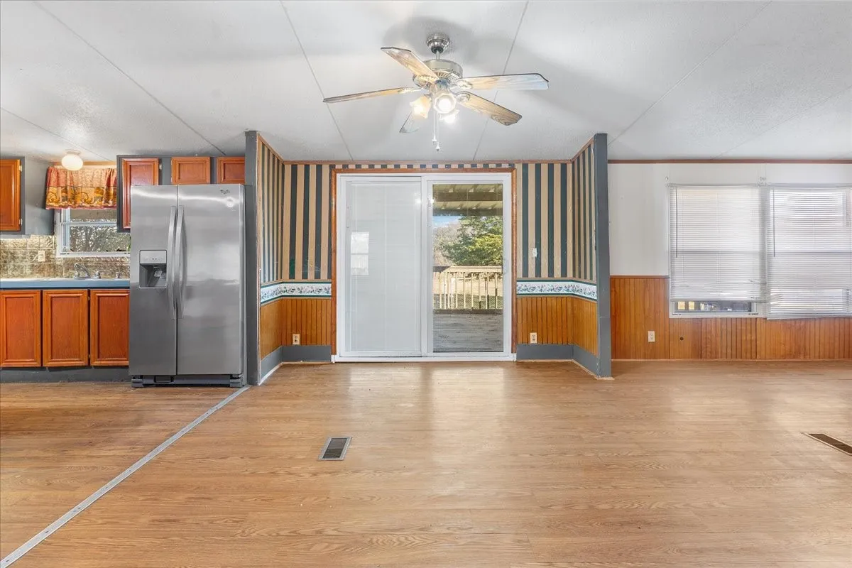 Kitchen featuring stainless steel fridge with ice dispenser, brown cabinets, a ceiling fan, light wood-style floors, and wainscoting