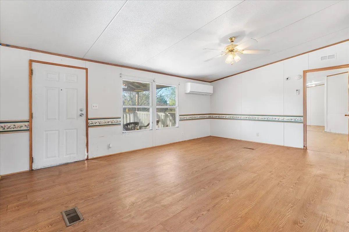 Unfurnished room featuring light wood finished floors, crown molding, lofted ceiling, a ceiling fan, and an AC wall unit