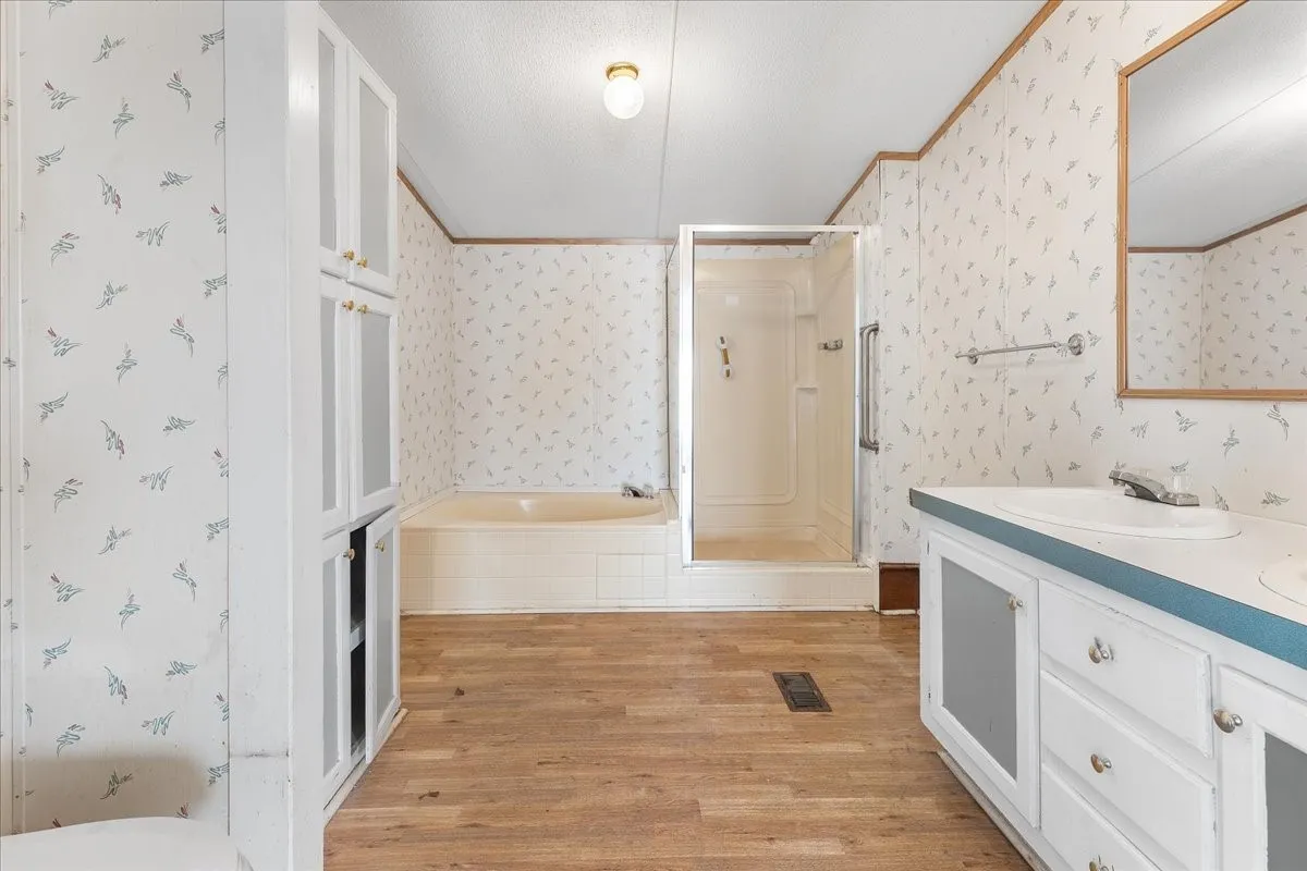 Full bathroom featuring wallpapered walls, a stall shower, light wood-style floors, double vanity, and tiled tub