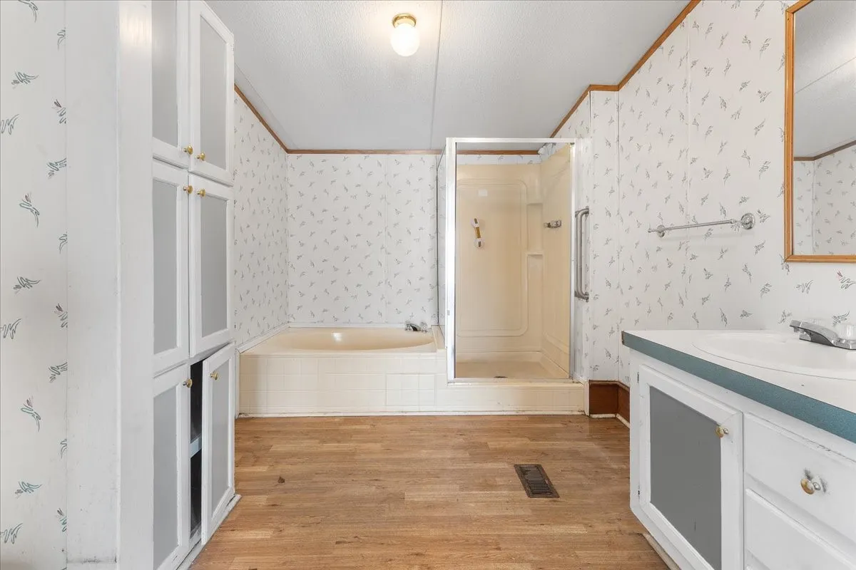 Bathroom featuring vanity, a stall shower, light wood-type flooring, wallpapered walls, and tiled tub
