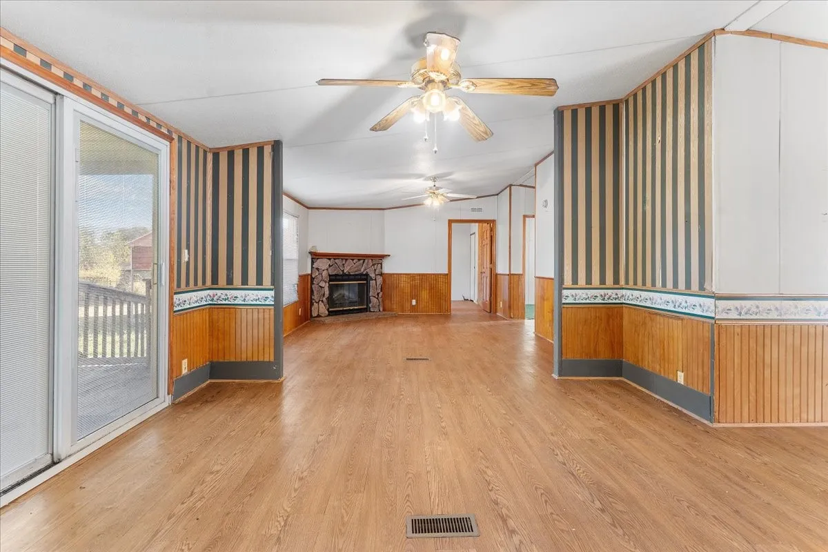 Unfurnished living room featuring wainscoting, wood walls, a stone fireplace, light wood-type flooring, and wallpapered walls