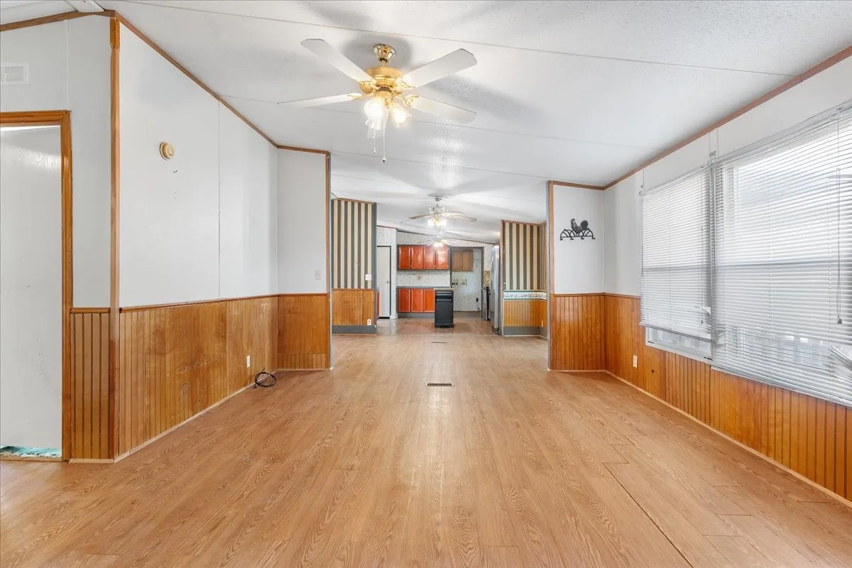 Unfurnished living room with wood walls, wainscoting, wood finished floors, ceiling fan, and ornamental molding