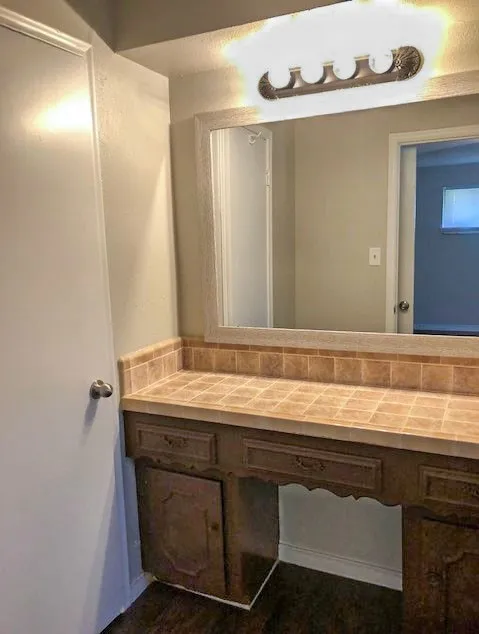 Vanity area featuring a tiled countertop, wood-finish cabinetry, and an overhead four-light fixture