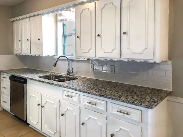 Kitchen featuring white cabinetry with decorative molding, dark speckled countertops, subway tile backsplash, and a double basin stainless steel sink with a pull-down faucet