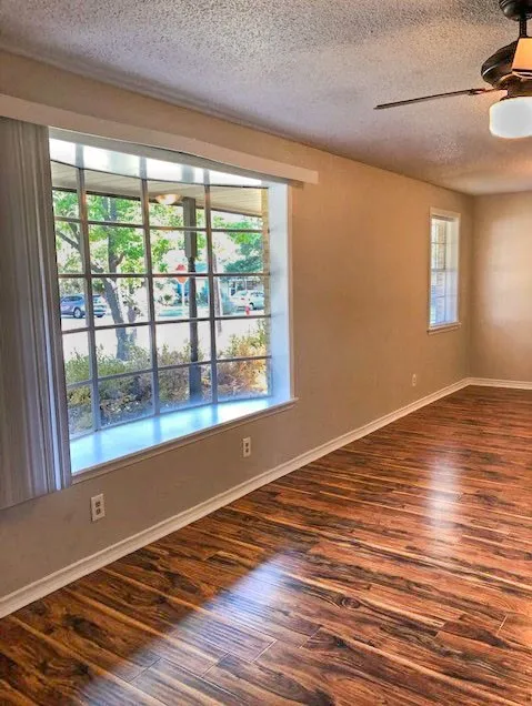 Spacious room featuring rich wood-finish flooring, a prominent bay window, and neutral wall tones