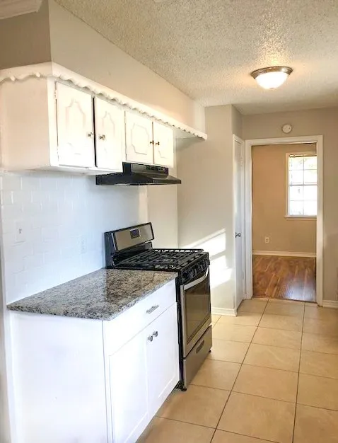 Kitchen featuring white cabinetry, speckled countertops, tile flooring, and a stainless steel gas range
