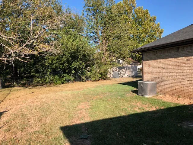 Expansive lawn area featuring mature trees and a brick exterior with a dark shingle roof