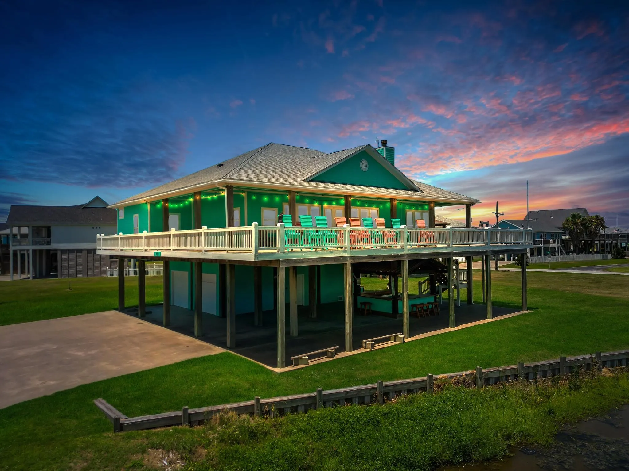 Striking elevated residence featuring a bold green exterior with white trim and wraparound covered porch