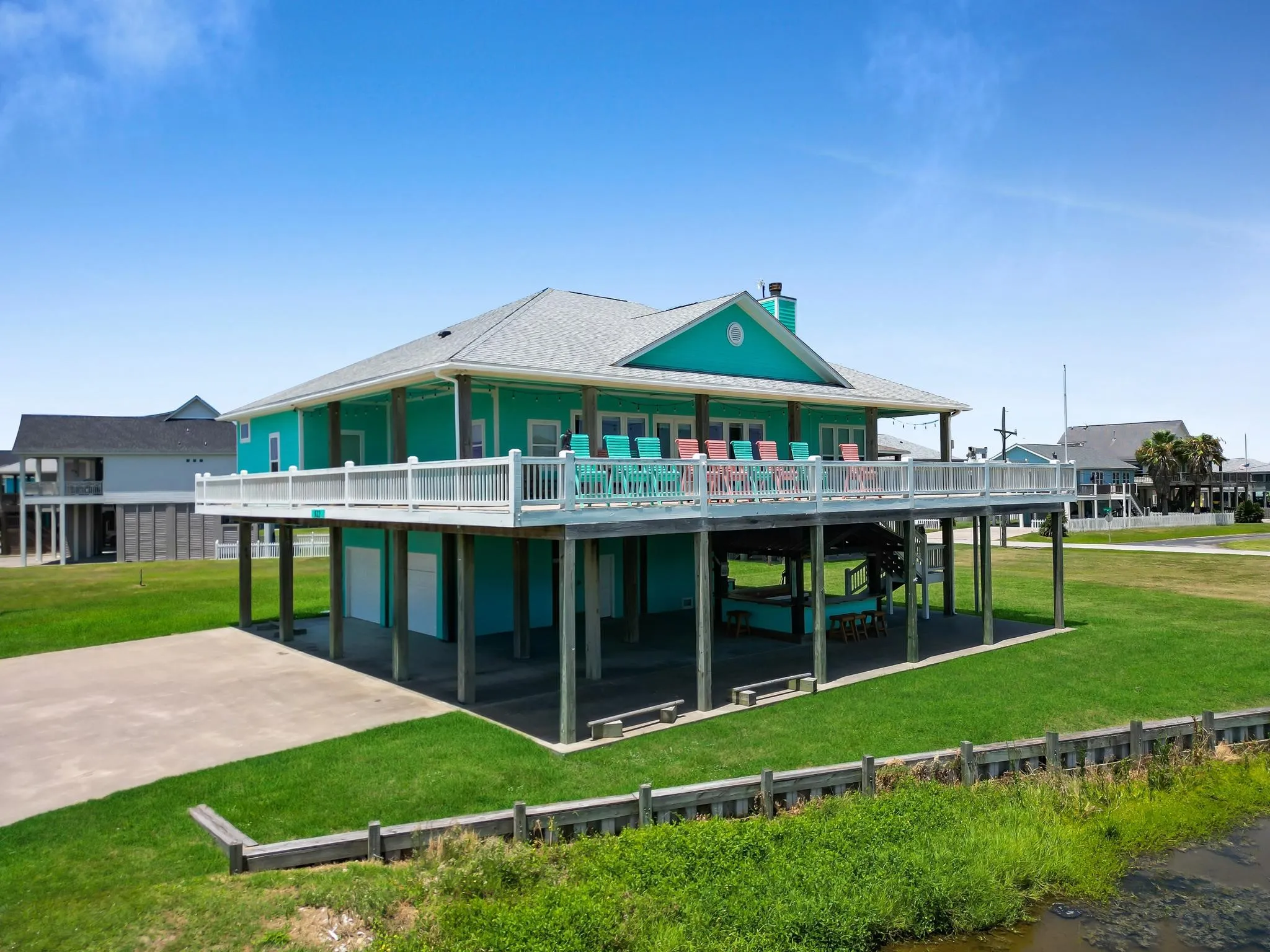 Elevated residence featuring a broad wrap-around deck, covered patio space, and a manicured lawn