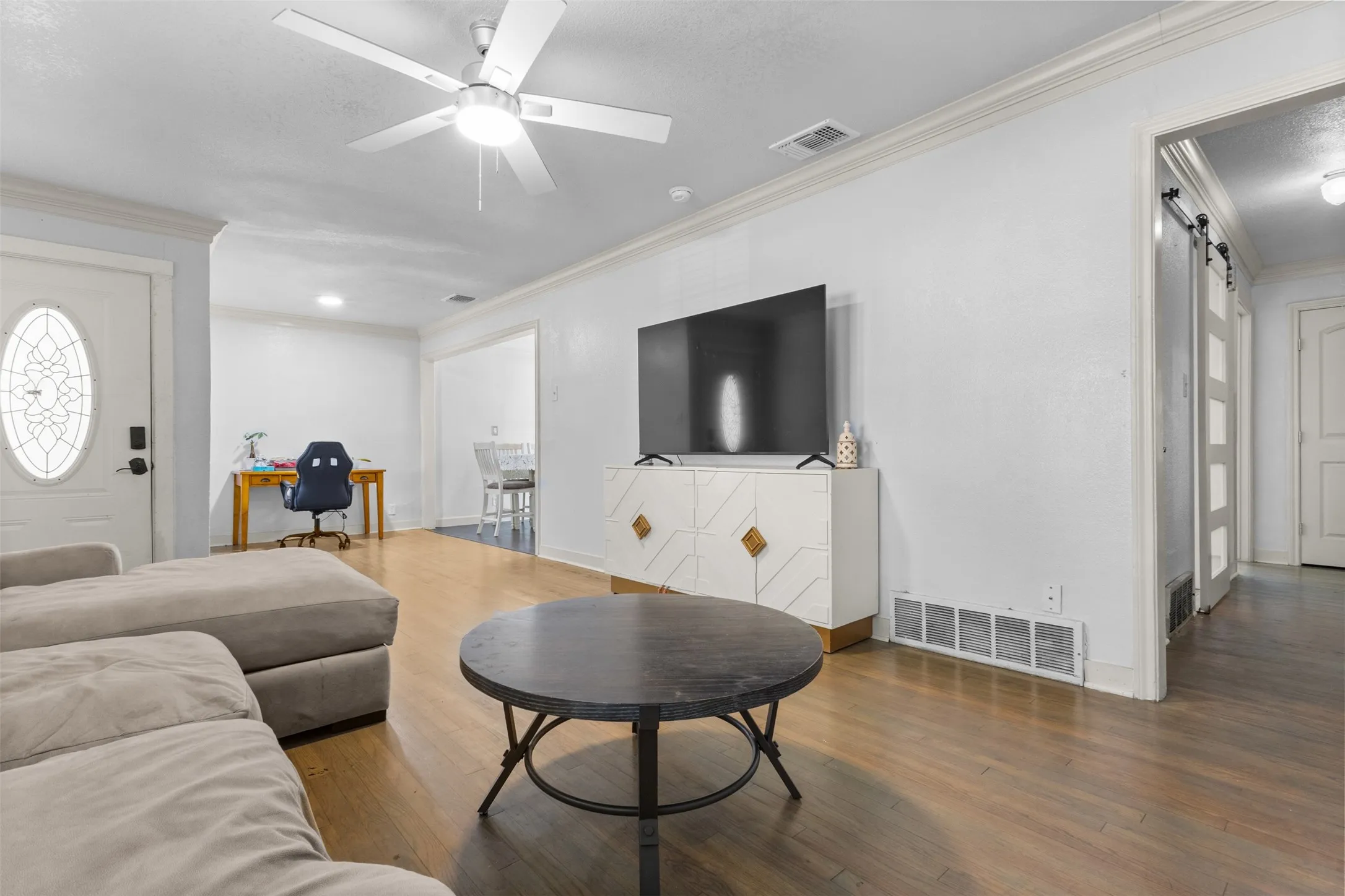 Living area featuring a barn door, wood finished floors, a desk, ceiling fan, and crown molding