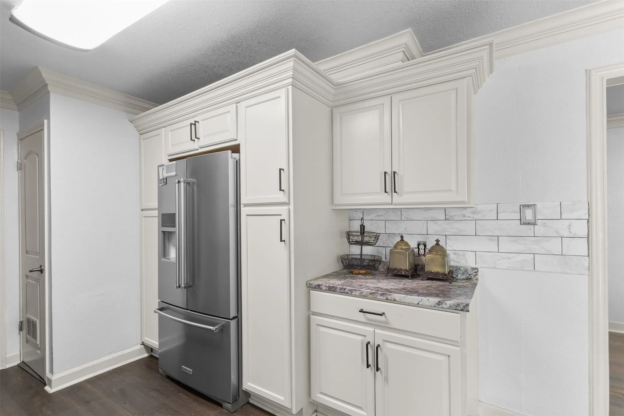 Kitchen featuring high end fridge, dark wood-style floors, decorative backsplash, ornamental molding, and white cabinetry