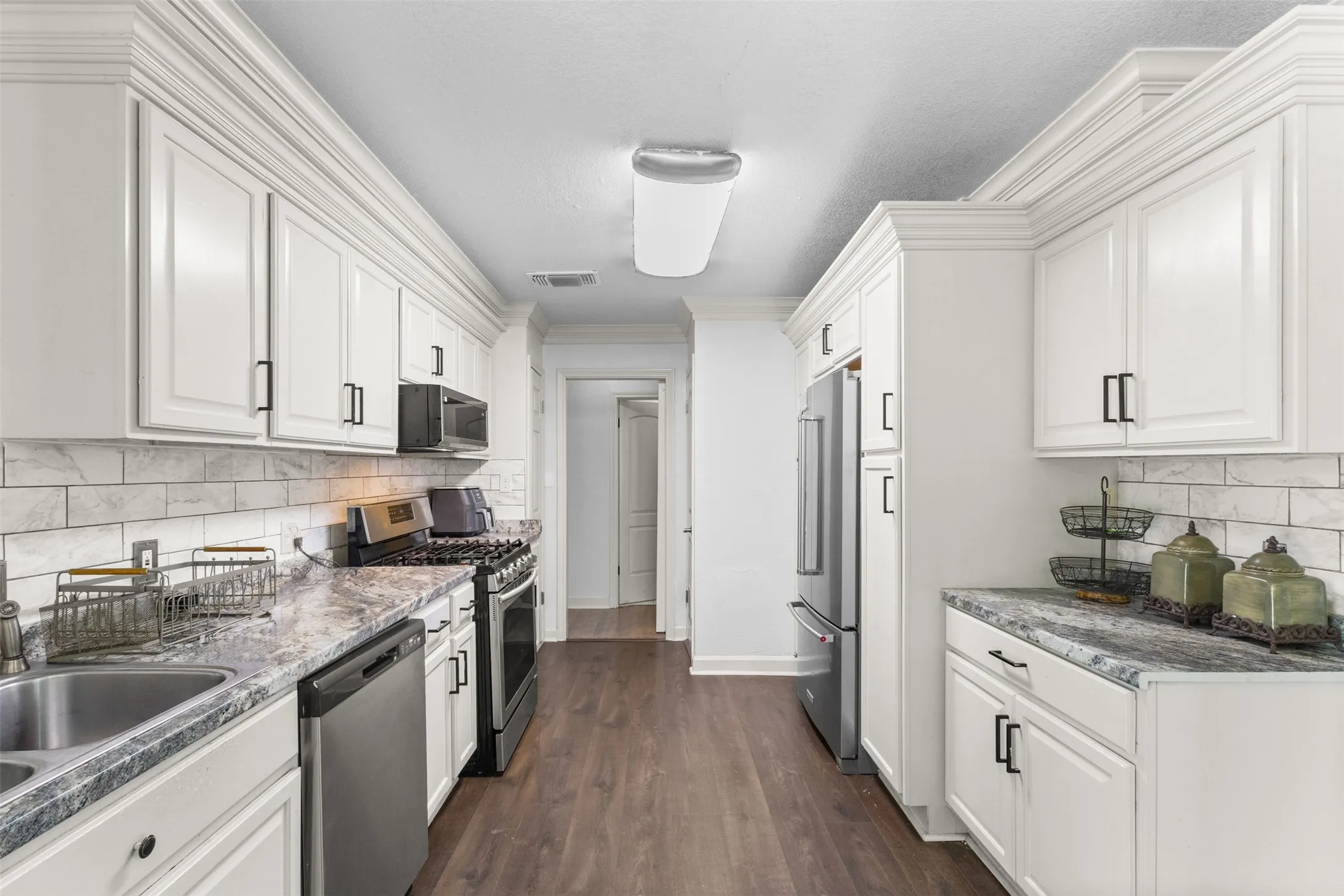 Kitchen featuring stainless steel appliances, decorative backsplash, white cabinets, dark wood-type flooring, and ornamental molding