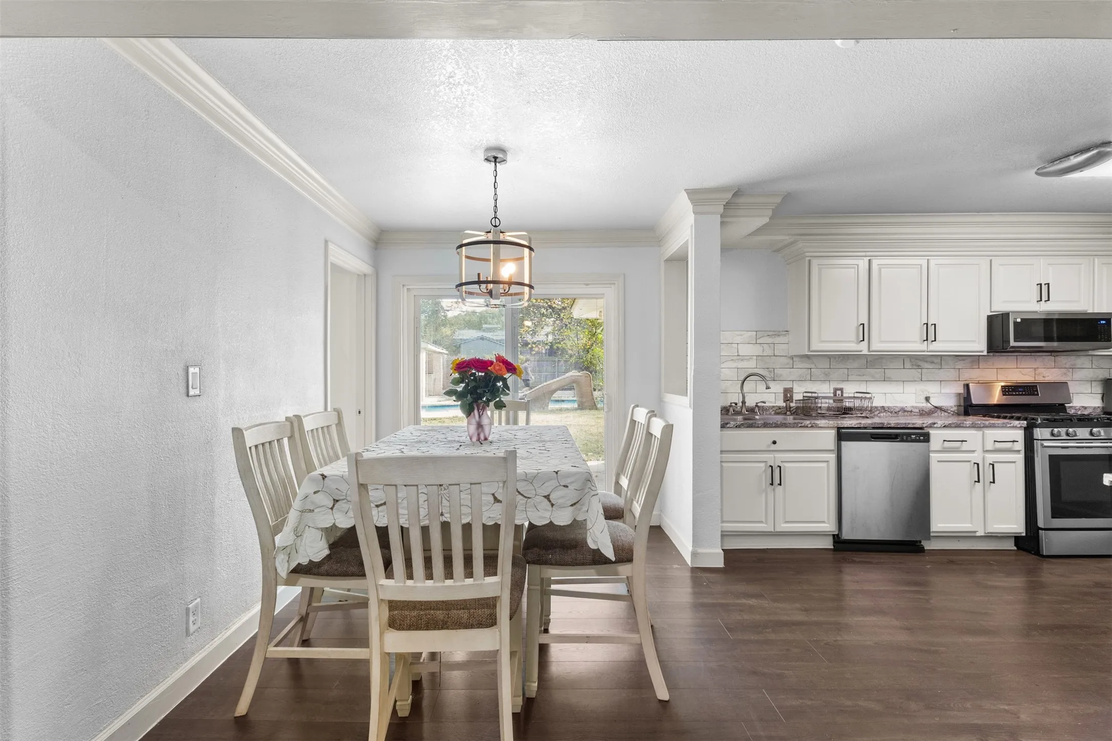 Dining area with dark wood-style flooring, ornamental molding, a chandelier, a textured ceiling, and a textured wall