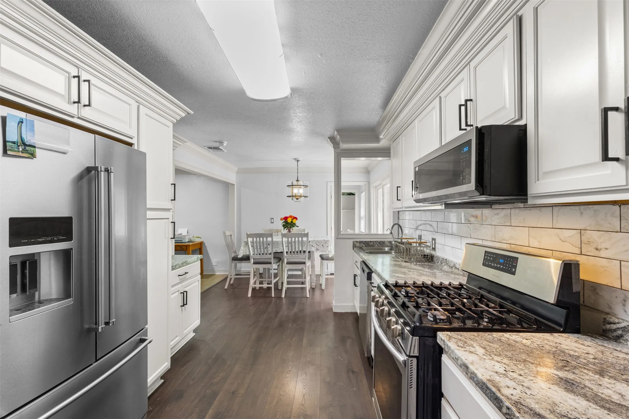 Kitchen featuring appliances with stainless steel finishes, decorative light fixtures, light stone counters, dark wood-type flooring, and ornamental molding