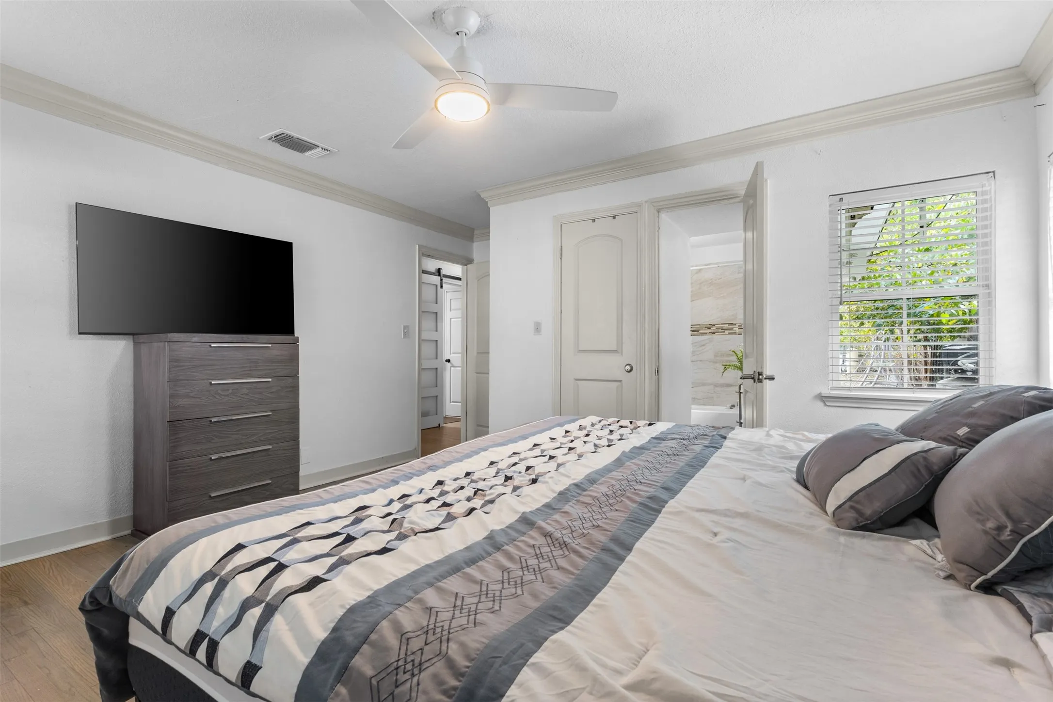Bedroom featuring crown molding, a ceiling fan, wood-type flooring, a barn door, and ensuite bath
