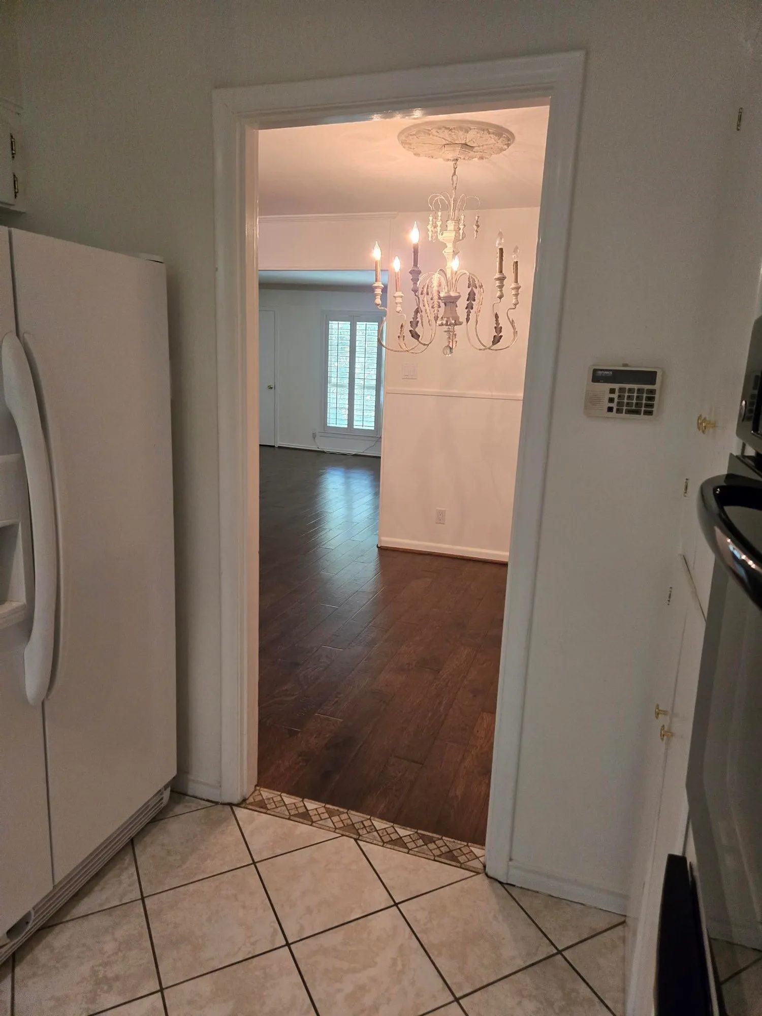 Tiled flooring with decorative border, wood-finish flooring, chandelier with decorative ceiling medallion, and plantation shutters