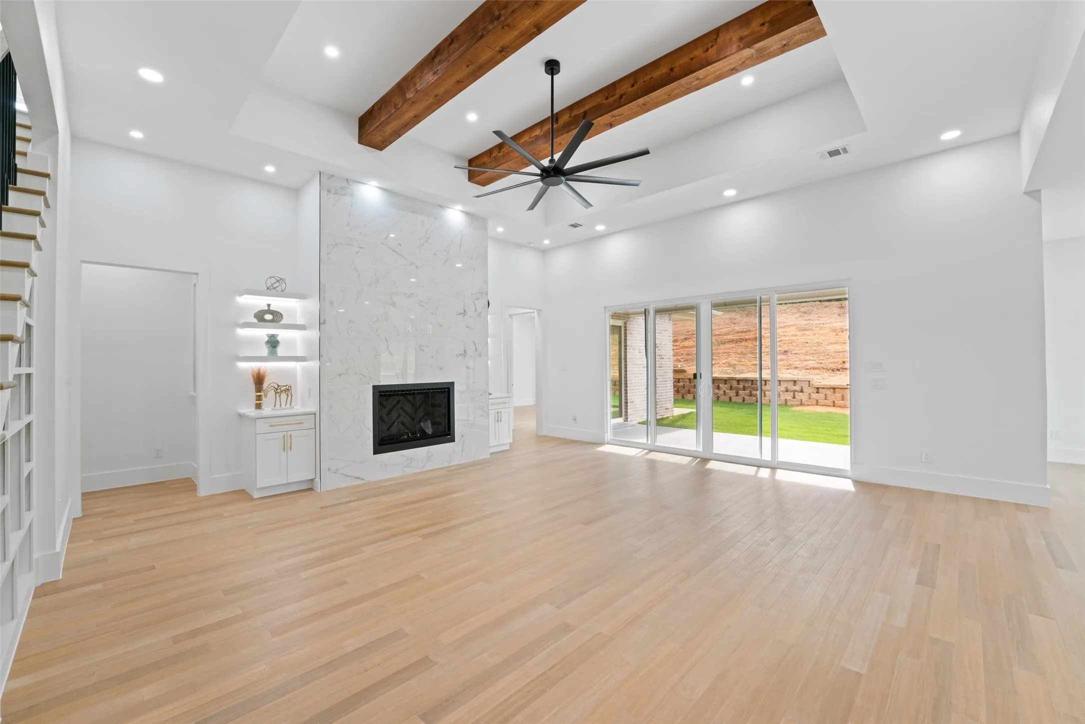 Unfurnished living room with a towering ceiling, beam ceiling, light wood-style flooring, a ceiling fan, and a fireplace