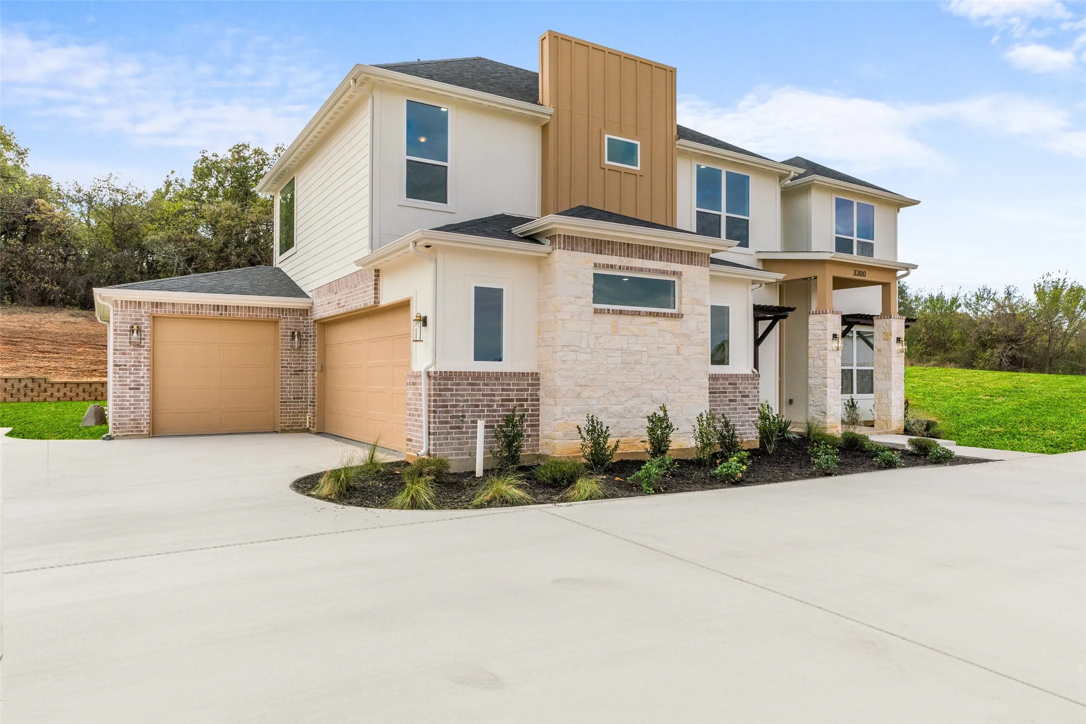 View of front facade with board and batten siding, driveway, stone siding, an attached garage, and roof with shingles
