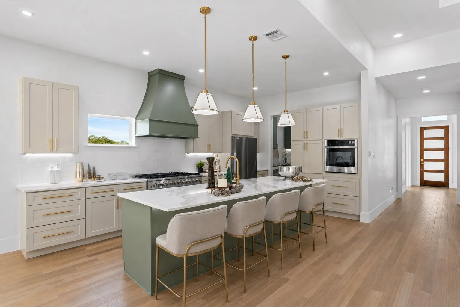 Gourmet kitchen featuring a large central island with seating, stainless steel appliances, a custom green range hood, light-toned cabinetry, and wood-finish flooring