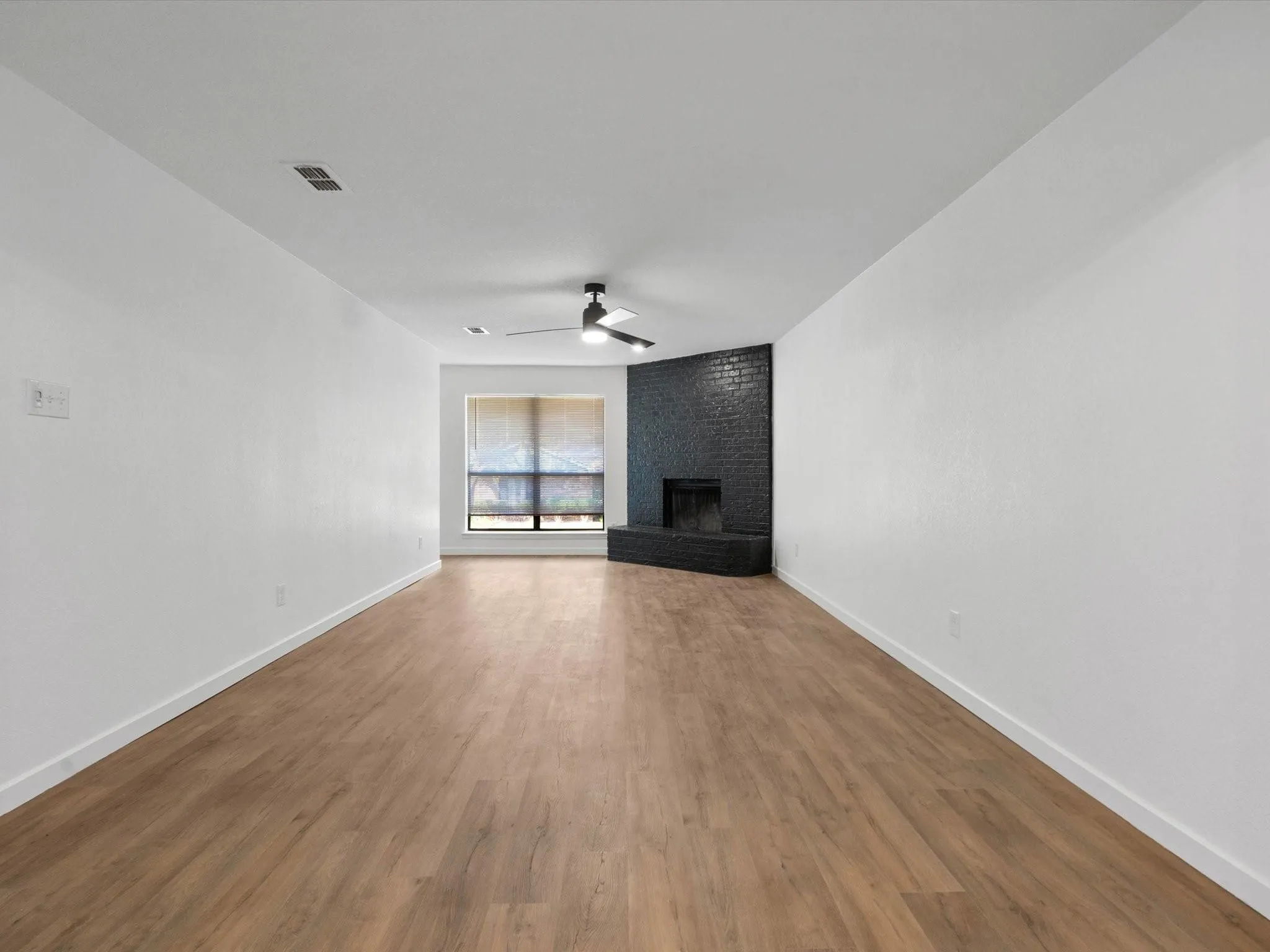 Unfurnished living room with a brick fireplace, wood finished floors, and a ceiling fan