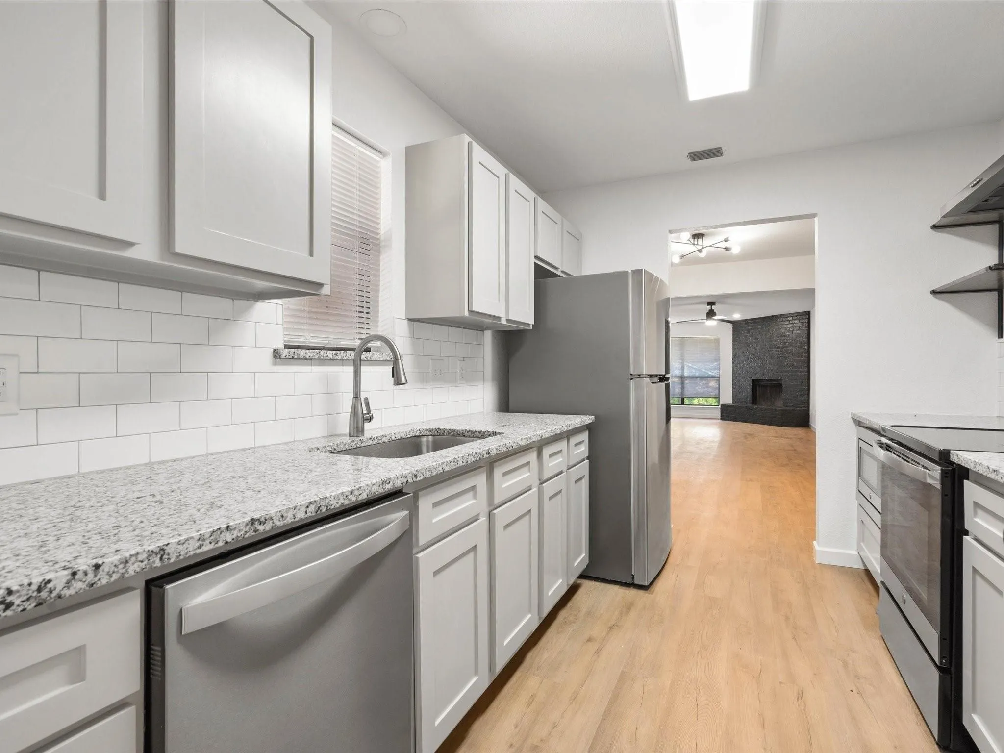 Kitchen with stainless steel appliances, light stone countertops, light wood-type flooring, backsplash, and ceiling fan