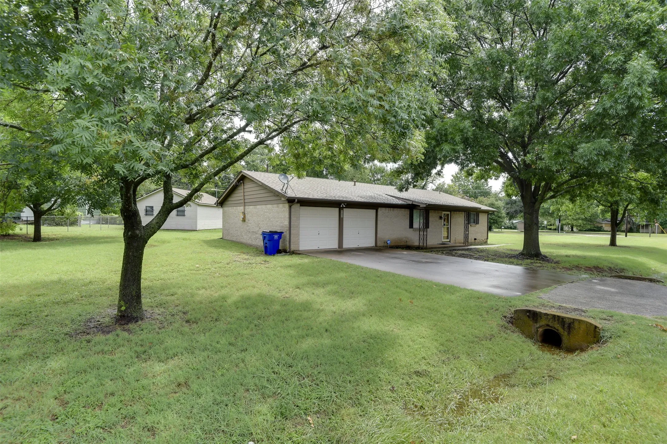 View of front of house featuring concrete driveway, an attached garage, a front lawn, brick siding, and view of wooded area