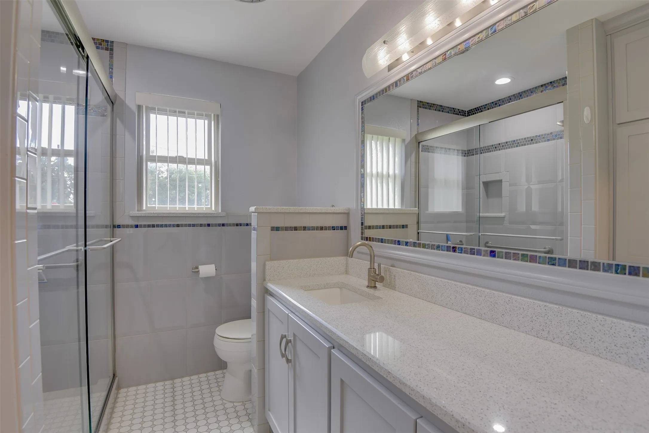 Full bath with vanity, healthy amount of natural light, a stall shower, light tile patterned floors, and tile walls