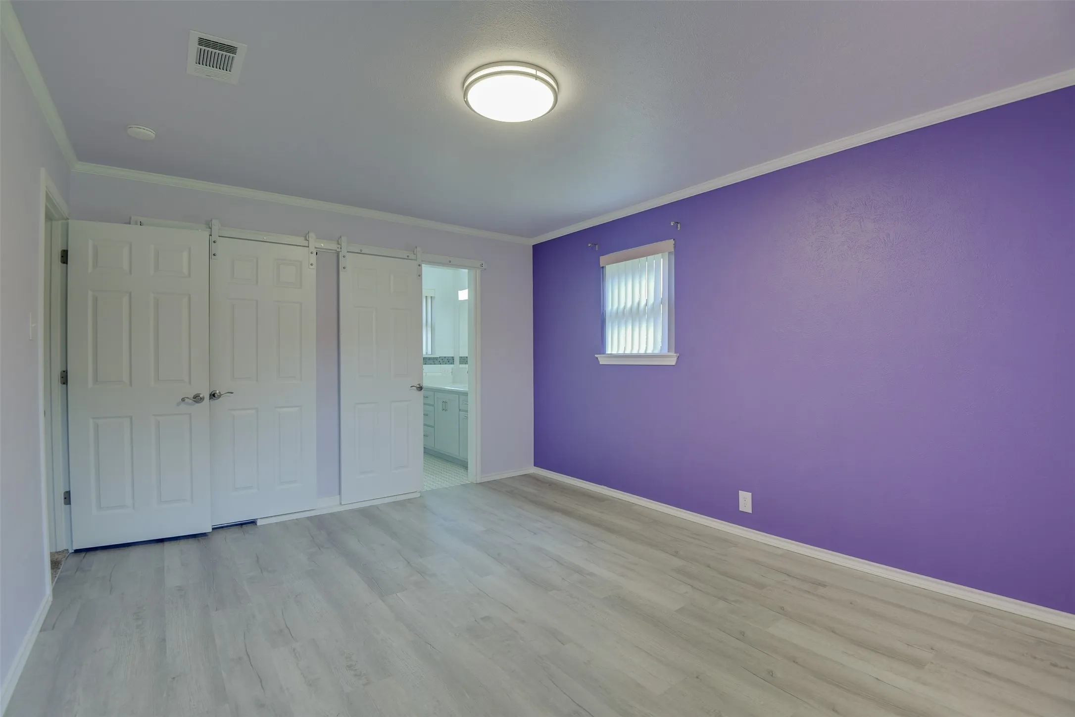 Unfurnished bedroom featuring crown molding, wood finished floors, connected bathroom, and a closet