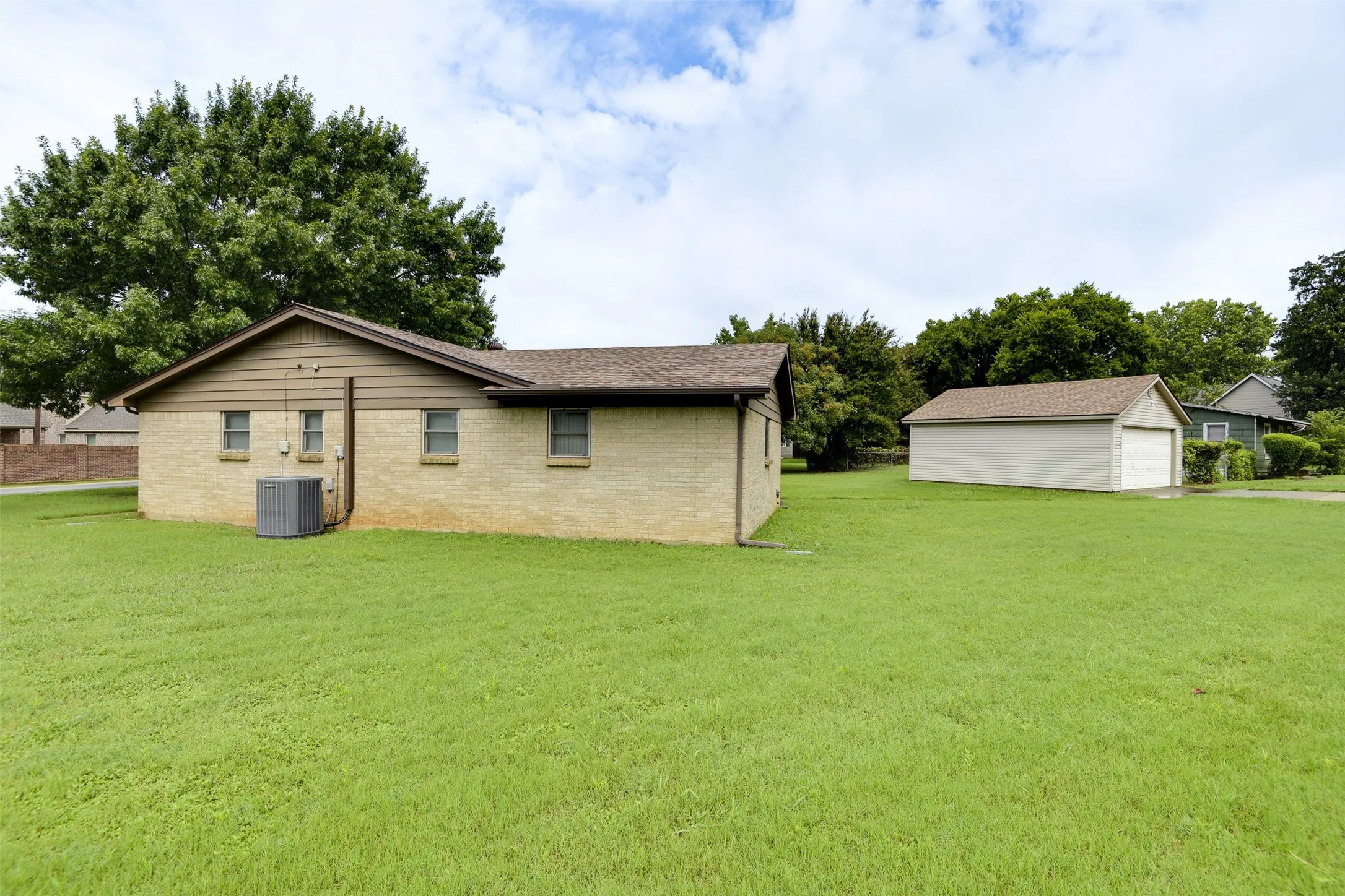Back of house with a yard, brick siding, a garage, an outdoor structure, and a shingled roof