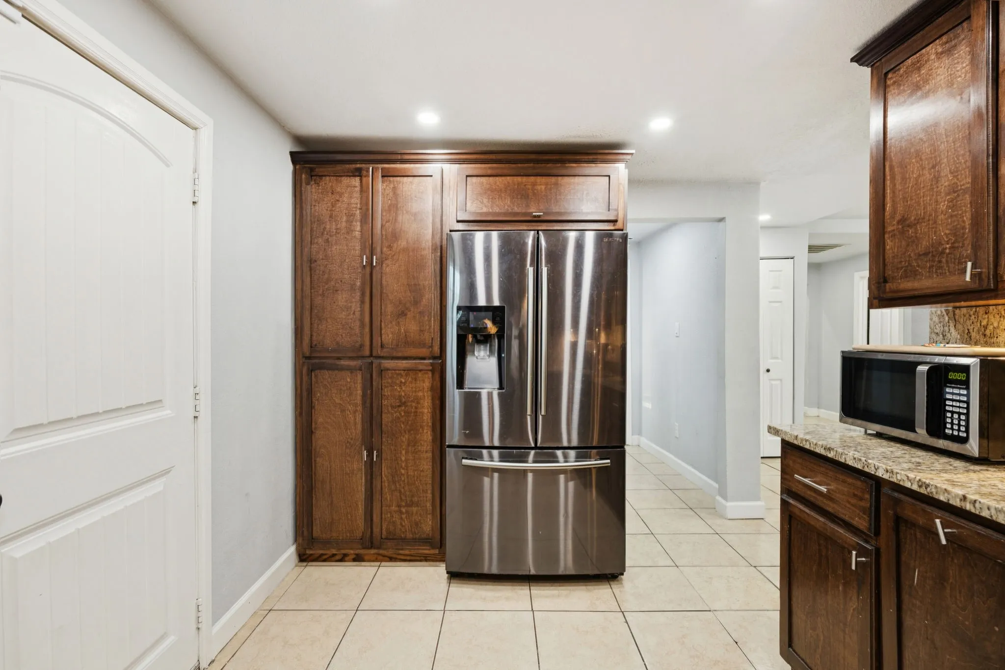 Kitchen with appliances with stainless steel finishes, light stone countertops, light tile patterned flooring, recessed lighting, and dark brown cabinets