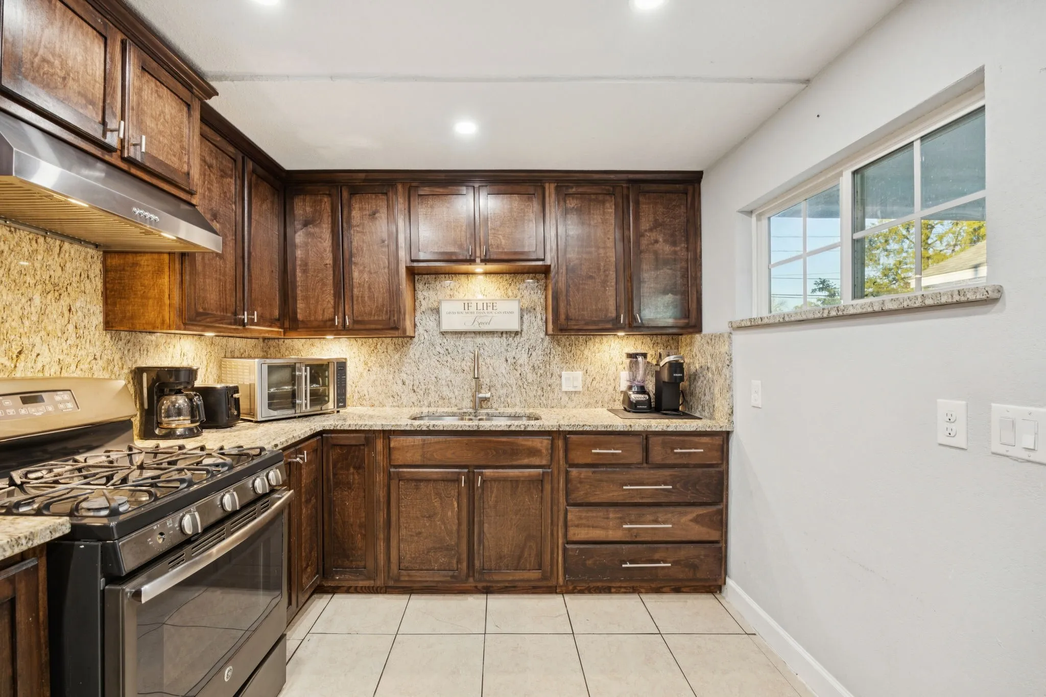 Kitchen featuring gas range oven, dark brown cabinets, tasteful backsplash, light stone countertops, and recessed lighting