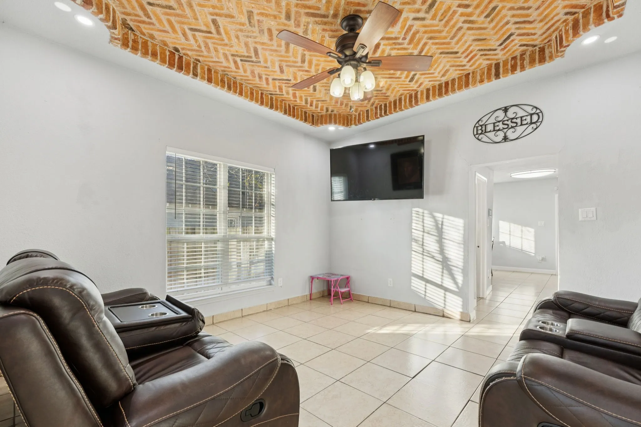 Living room featuring brick ceiling, ceiling fan, a tray ceiling, and light tile patterned floors