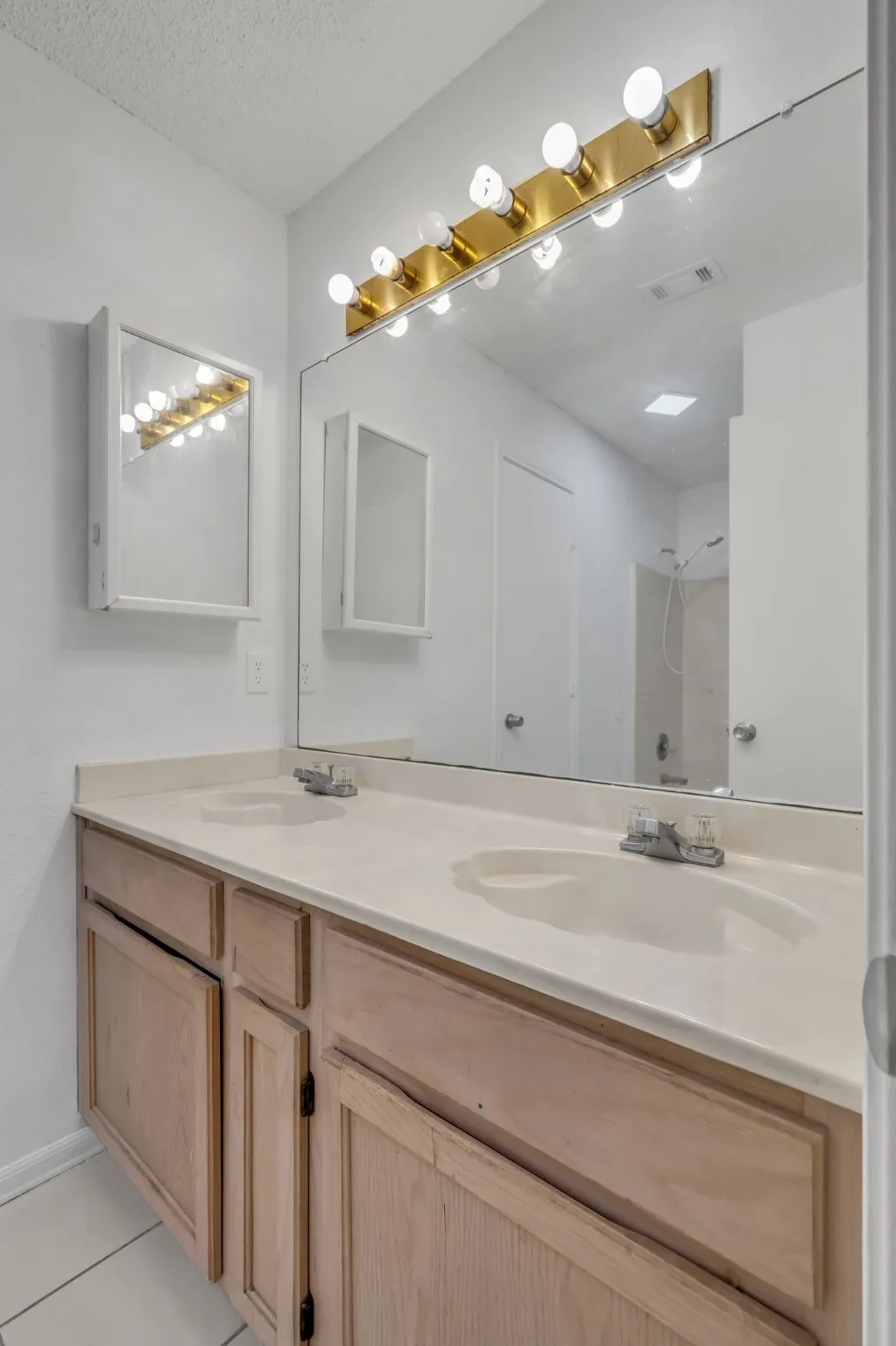 Bathroom with double vanity, light tile patterned floors, a textured ceiling, and a shower