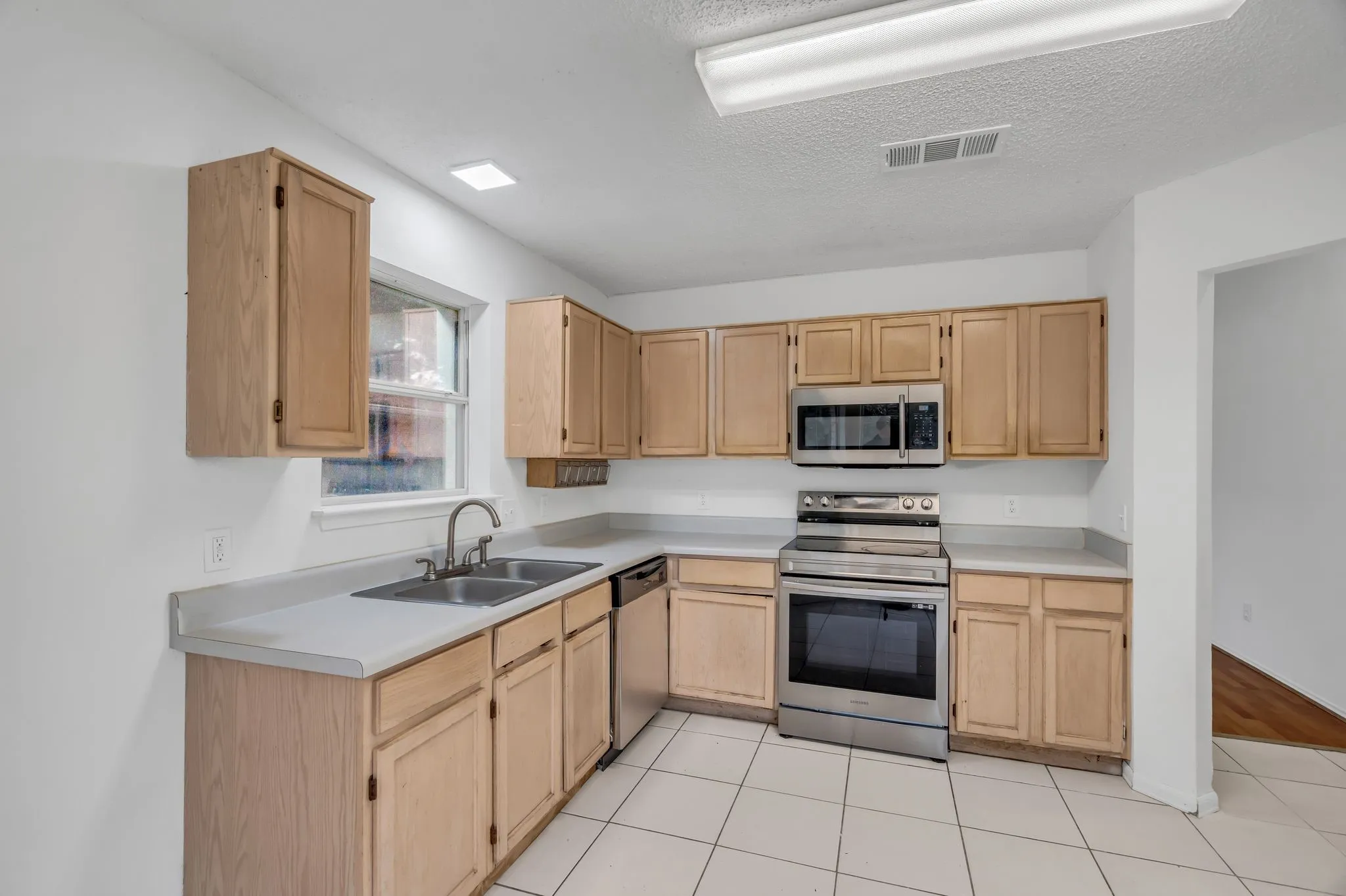 Kitchen featuring light brown cabinets, stainless steel appliances, light countertops, a textured ceiling, and light tile patterned floors