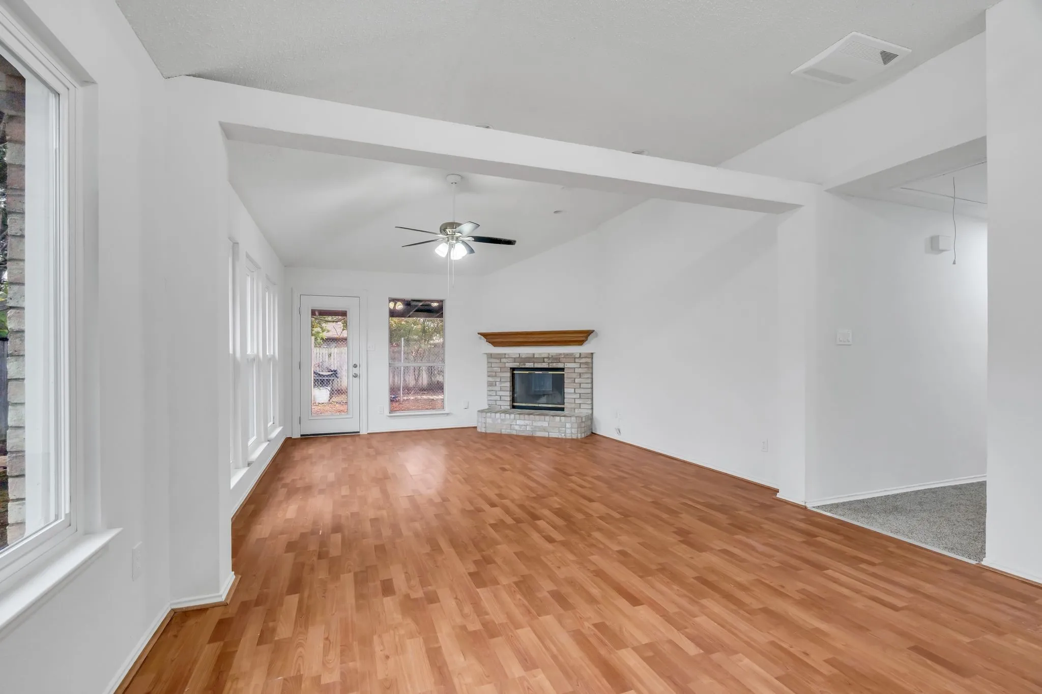 Unfurnished living room with a ceiling fan, a fireplace, light wood finished floors, and vaulted ceiling