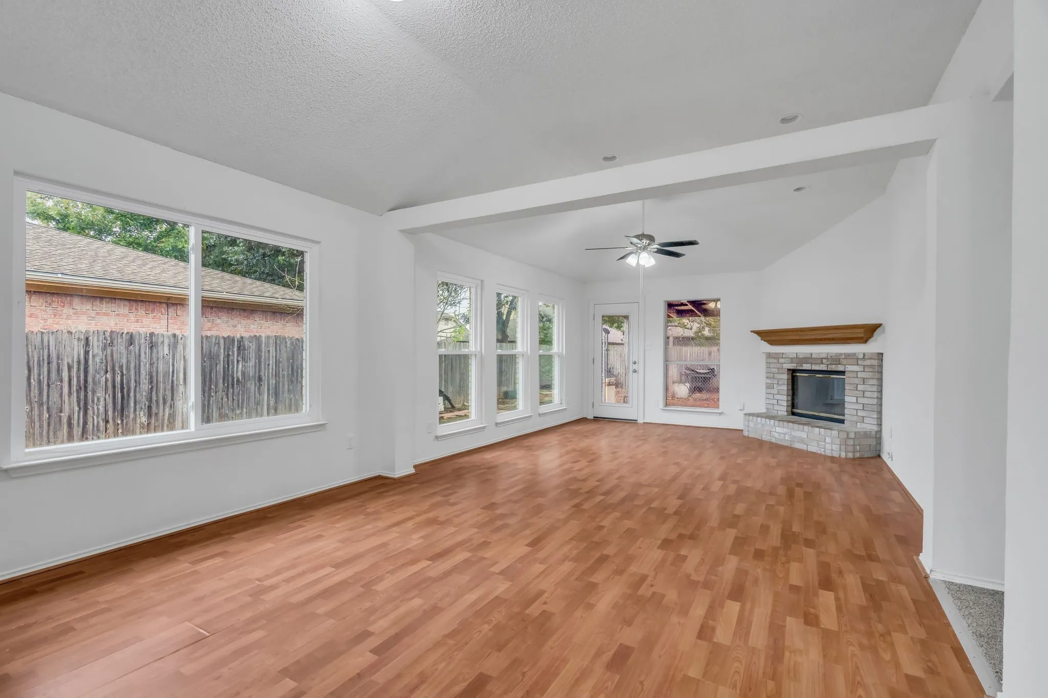 Unfurnished living room featuring a brick fireplace, light wood finished floors, lofted ceiling, ceiling fan, and a textured ceiling